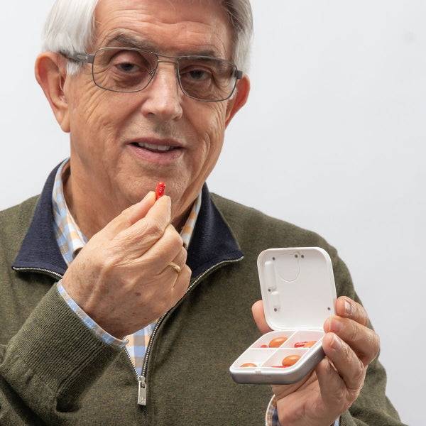 Bărbat senior pregătit să ia o pastilă din cutia inteligentă Pilly Inovamarket, cu funcție de alarmă și vibrație pentru mementouri eficiente.